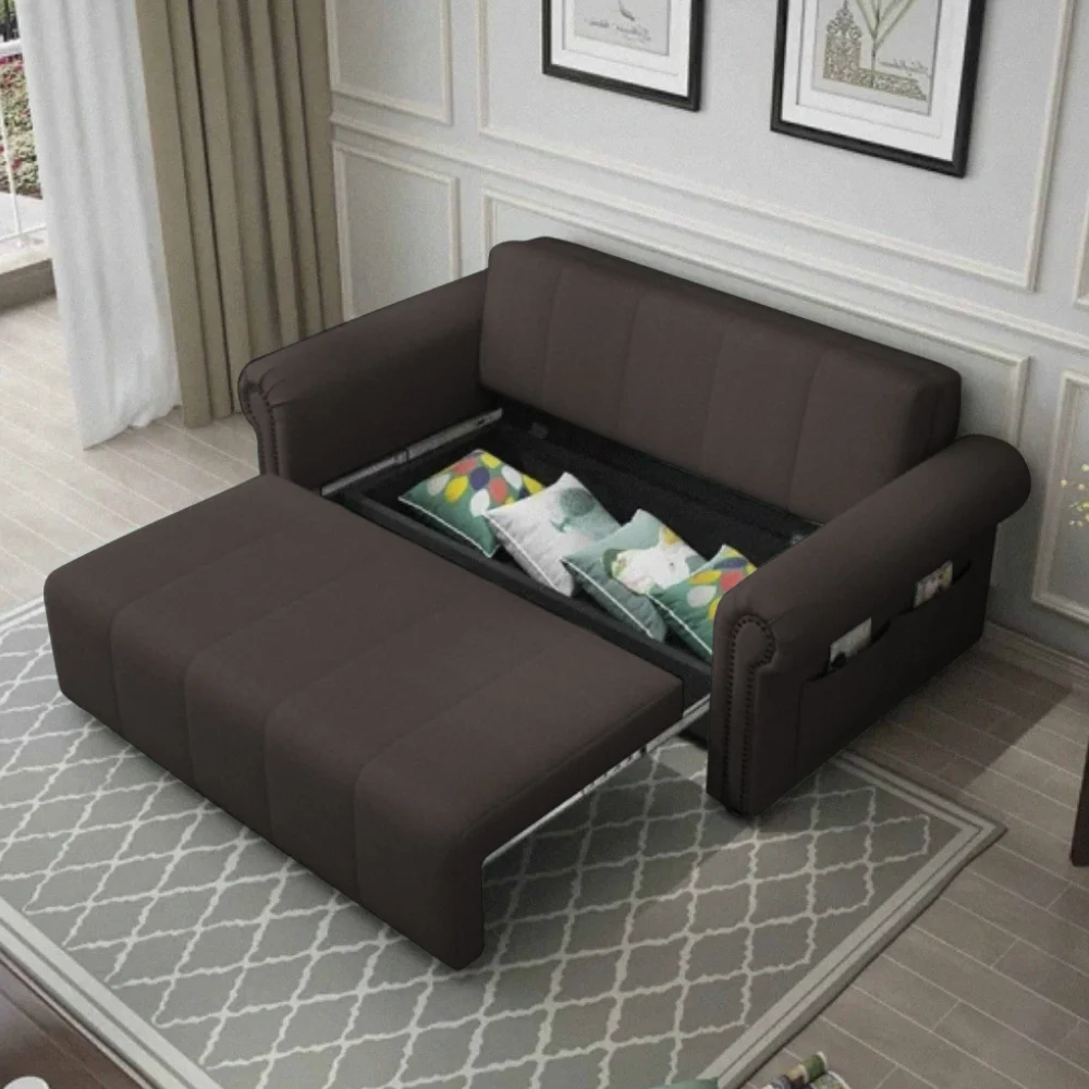 A dark brown pull-out sofa bed in a classic living room setting, extended to show the sleeping surface and internal storage for decorative pillows, featuring armrest storage pockets.
