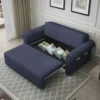 A dark blue pull-out sofa bed in a living room, with the bottom extended and revealing a storage compartment filled with decorative pillows, and side pockets on the armrests