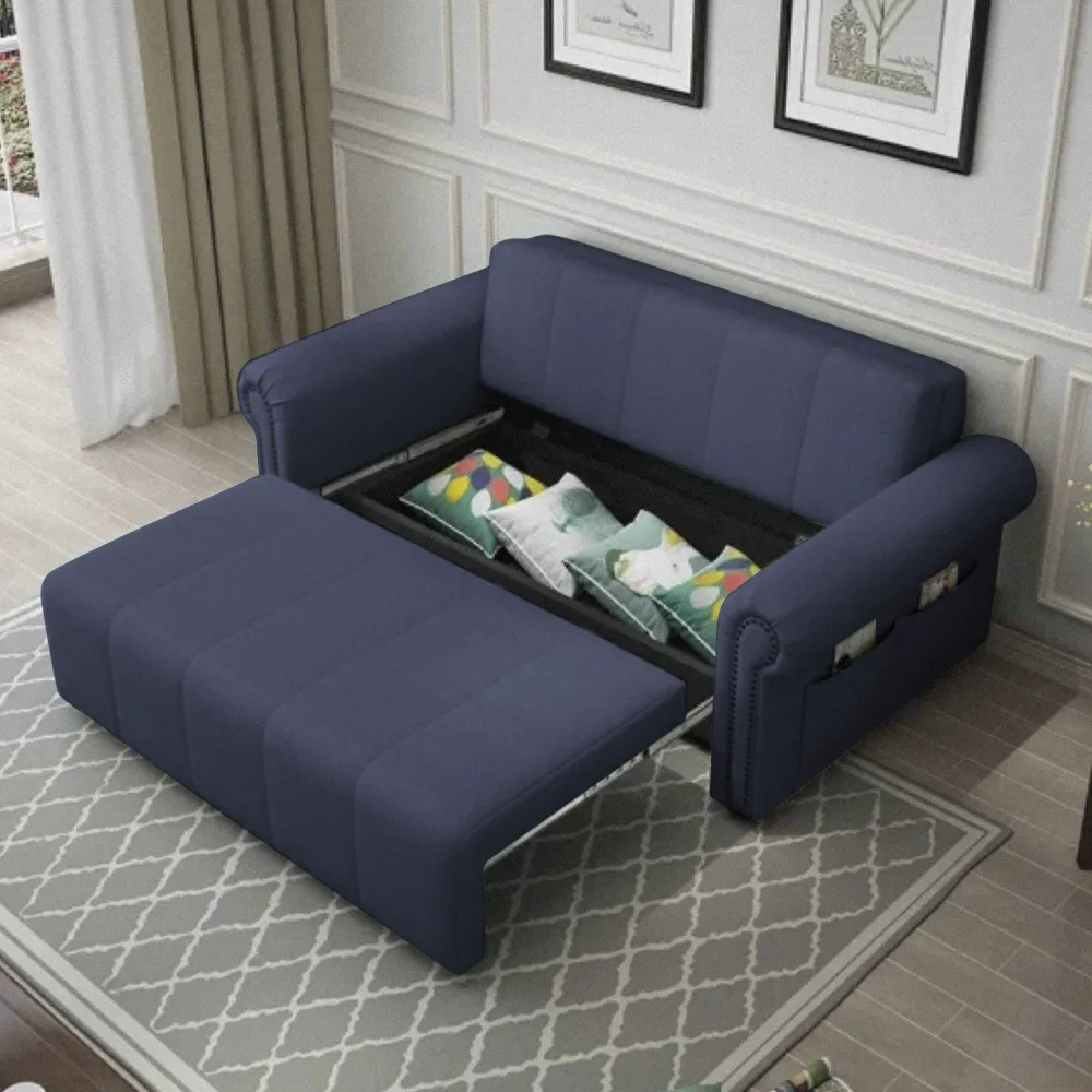A dark blue pull-out sofa bed in a living room, with the bottom extended and revealing a storage compartment filled with decorative pillows, and side pockets on the armrests