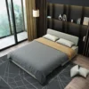 Bambillo Citta Armless Sofa Bed With Headboard in light grey fabric colour, showing bed configuration with dark grey doona on bed and two light grey pillows